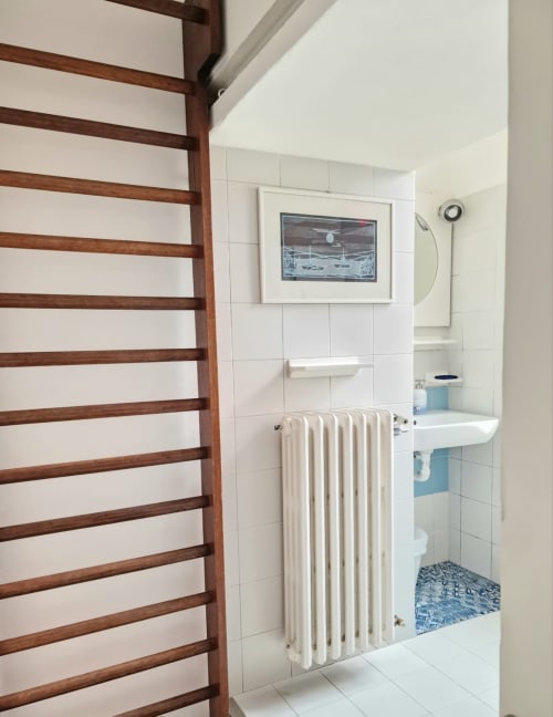 Bagno con piastrelle bianche, radiatore, lavandino e quadro costiero incorniciato al B&B del Podestà a Fabriano