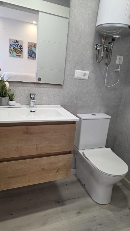 Baño moderno en la casita Siesta 9 de Monica Socarici, Oropesa. Inodoro blanco, tocador de madera, azulejos grises, espejo y