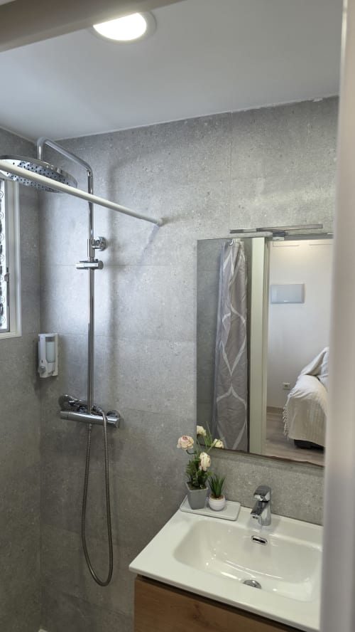 Baño moderno con ducha de azulejos grises, lavabo blanco y espejo en la casa rural MONICA SOCARICI en Benicàssim