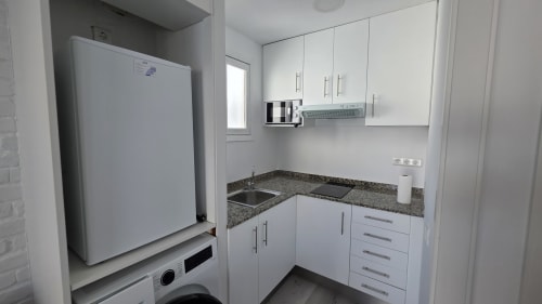Cocina moderna blanca con encimera de granito, fregadero, electrodomésticos y refrigerador en la casita Siesta 9, Benicàssim
