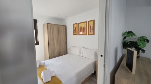 Dormitorio luminoso en la casa de huéspedes Monica Socarici, Benicàssim, con cama queen, sábanas blancas, armario de madera y planta en maceta