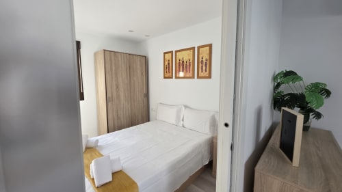 Habitación luminosa en la casa rural MONICA SOCARICI, Benicàssim, con cama blanca, armario de madera y planta verde en la mesilla de noche