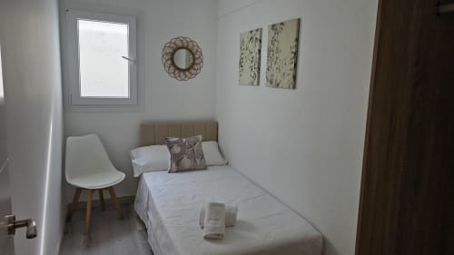 Dormitorio luminoso en el apartamento Monica Socarici en Oropesa con cama, silla blanca, espejo decorativo y arte mural