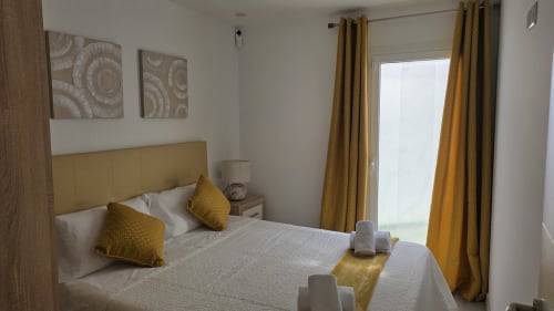 Habitación moderna en Monica Socarici, Benicàssim con cabecero amarillo, cortinas y almohadas color mostaza, ropa de cama blanca