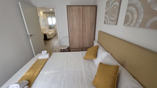 Dormitorio moderno en casa rural de Benicàssim con cama queen, almohadas doradas, armario de madera y baño privado