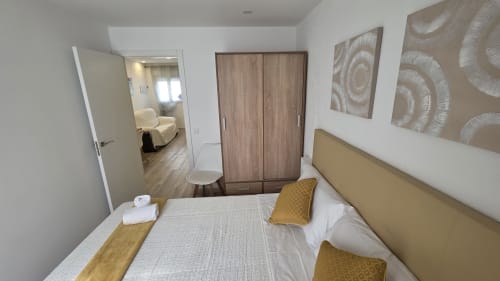 Dormitorio moderno con cabecero dorado en el hotel Monica Socarici de Benicàssim, armario de madera y distribución abierta hacia la sala de estar