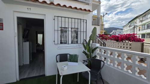 Patio de bungalow frente al mar con muebles blancos, plantas en maceta y vibrantes flores de buganvilia roja