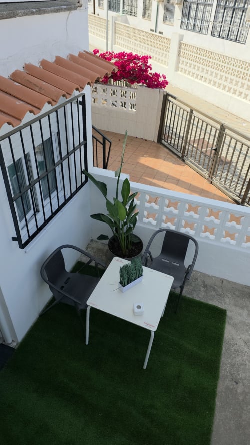 Patio de bungalow frente al mar en Monica Socarici con césped artificial, mesa blanca, sillas negras y buganvilia magenta vibrante