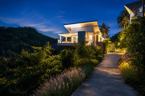 Villa Indigo moderne à Samui au coucher du soleil, illuminée de lumières chaudes, entourée de jardins tropicaux luxuriants et de palmiers à Koh
