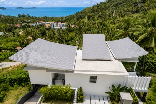 Vue aérienne de la Villa Indigo Samui : architecture blanche moderne, toitures grises, jardins tropicaux et océan turquoise à Koh