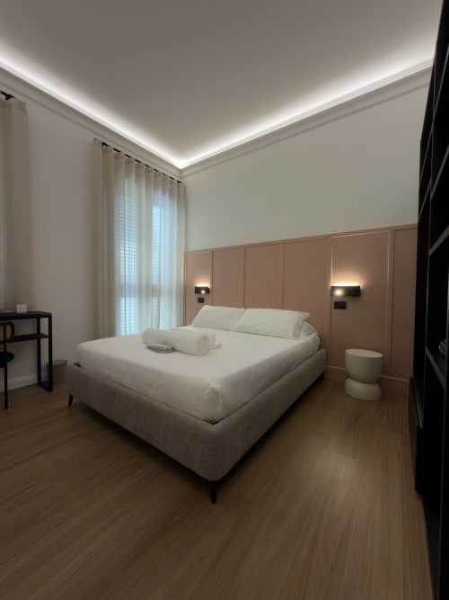 Camera moderna a Maison Riviera a Reggio di Calabria con letto bianco, testata in terracotta, illuminazione indiretta e pavimenti in legno