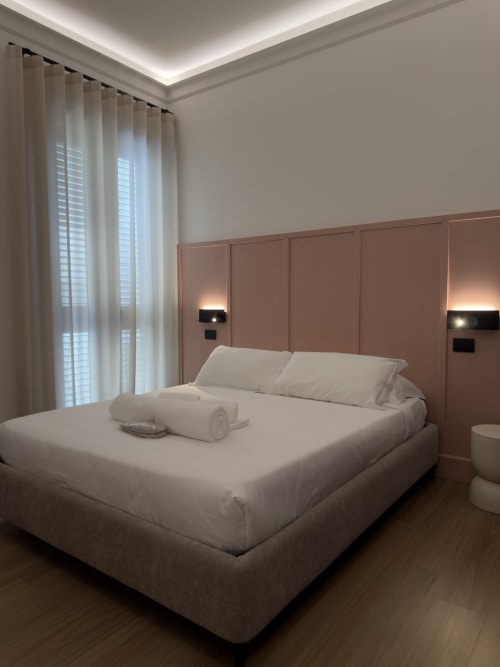 Moderna camera matrimoniale presso Maison Riviera con testata in terracotta, biancheria bianca, tende e illuminazione ambientale dal soffitto