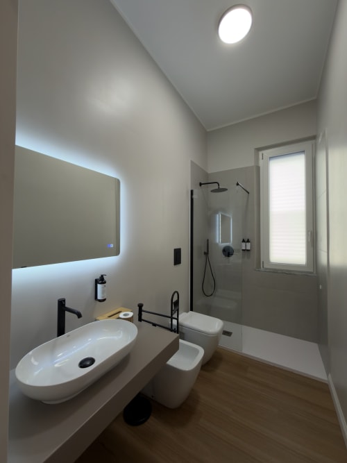 Bagno moderno a Maison Riviera con specchio illuminato, lavabo bianco a pozzo, toilette e doccia con box in vetro e rubinetteria nera