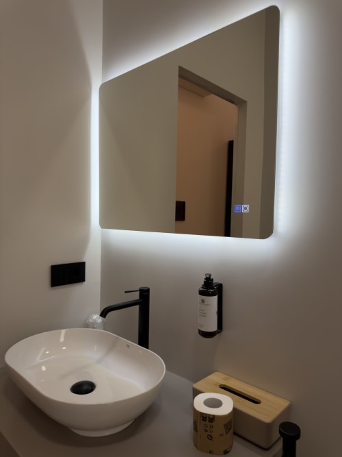 Bagno moderno a Maison Riviera con specchio illuminato, lavabo bianco in ceramica, rubinetto nero e accessori a Reggio di