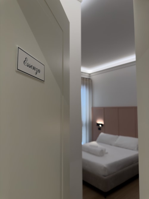 Ingresso della suite Essenza a Maison Riviera che mostra l'accesso alla moderna camera matrimoniale con letto, testiera in legno e illuminazione ambientale