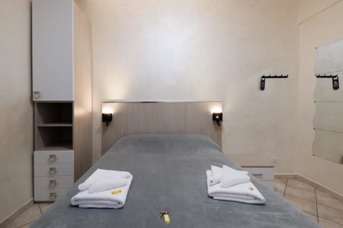 Camera moderna all'hotel ViOletta a Lido di Ostia con letto grigio, asciugamani bianchi, lampade a parete e spazi di ripostiglio.