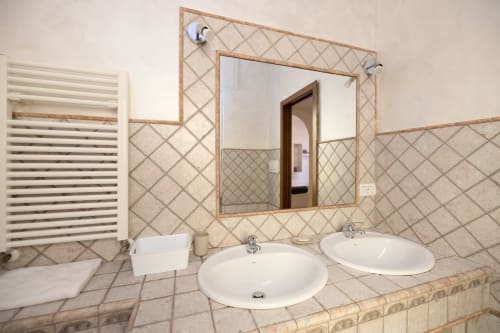 Bagno moderno dell'hotel ViOletta a Lido di Ostia con doppi lavabi tondi, specchio incorniciato e rivestimento in piastrelle diagonali