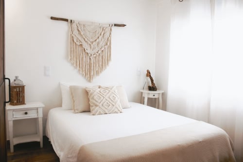Serene bedroom at Vila Vale Guest House with white linens, macramé wall hanging, and garden view in Charneca da Caparica