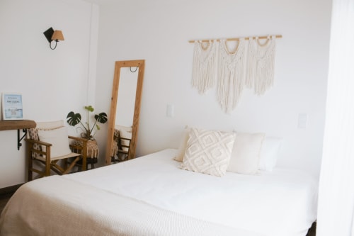 Quarto Land Suite da Vila Vale Guest House com roupa de cama branca, painel de macramé, espelho de madeira e decoração boho em Charneca