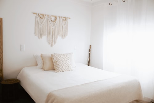 Quarto minimalista e luminoso na Vila Vale Guest House com roupa de cama branca, painel de macramê e decoração neutra em Charneca da