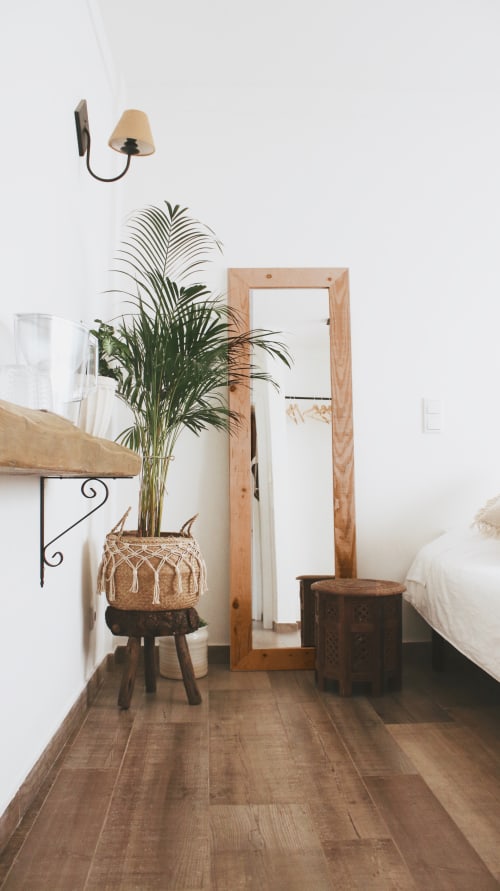 Quarto minimalista na Vila Vale Guest House com espelho de madeira, planta palmácea em vaso, luminária de parede e piso de madeira