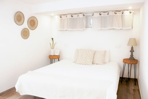 Quarto luminoso na Vila Vale Guest House com cama branca, almofadas creme, decoração em palha na parede e criados em madeira com luminárias