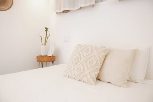 Quarto minimalista com almofadas creme, almofada com padrão geométrico, mesinha de madeira com planta na Vila Vale Guest House