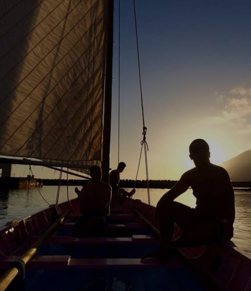 Silhouetted sailors on a traditional sailing boat at sunset in Madalena, Portugal