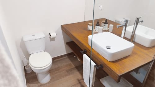 Banheiro moderno da Suíte Sunrise na Vila Vale Guest House com bancada em madeira, pia branca, sanitário e itens de higiene em Charneca