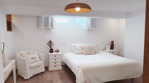 Quarto Sunrise Suite da Vila Vale Guest House com cama queen, poltrona creme, luminária de vime e criado branco