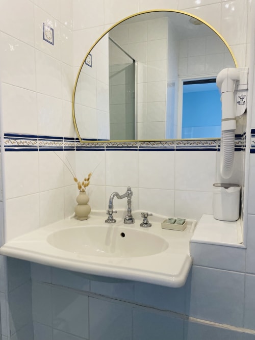 Salle de bain élégante avec miroir rond doré, lavabo blanc circulaire, robinetterie chromée et carreaux décoratifs à la Maison Nolette
