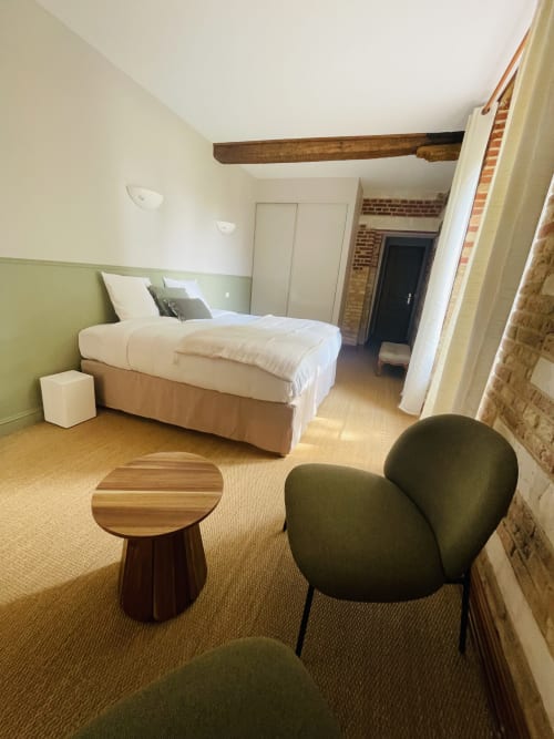 Suite moderne à la Maison Nolette avec lit, fauteuil vert, table de nuit en bois et poutre apparente à Noyelles sur Mer