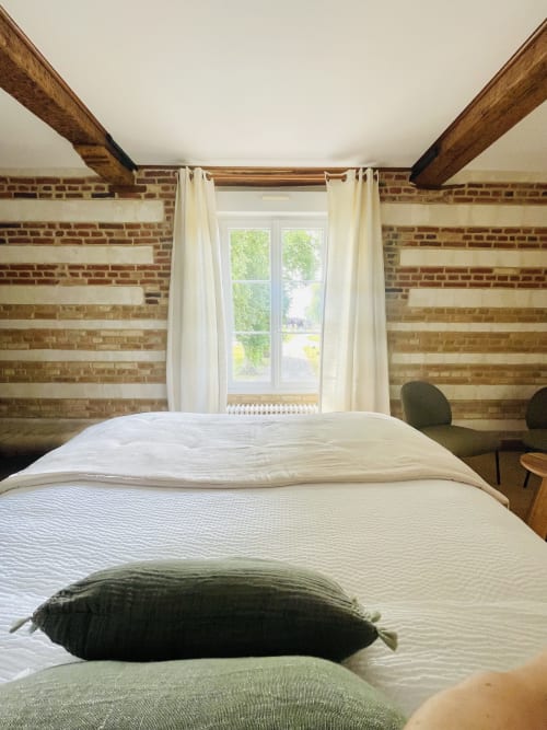 Chambre rustique avec poutres apparentes à la Maison Nolette, murs en brique, literie blanche, vue sur le jardin