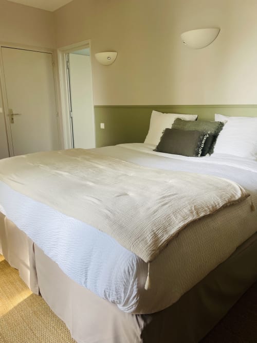 Spacieuse suite à Maison Nolette avec literie crème, tête de lit verte et vue sur le jardin à Noyelles sur Mer