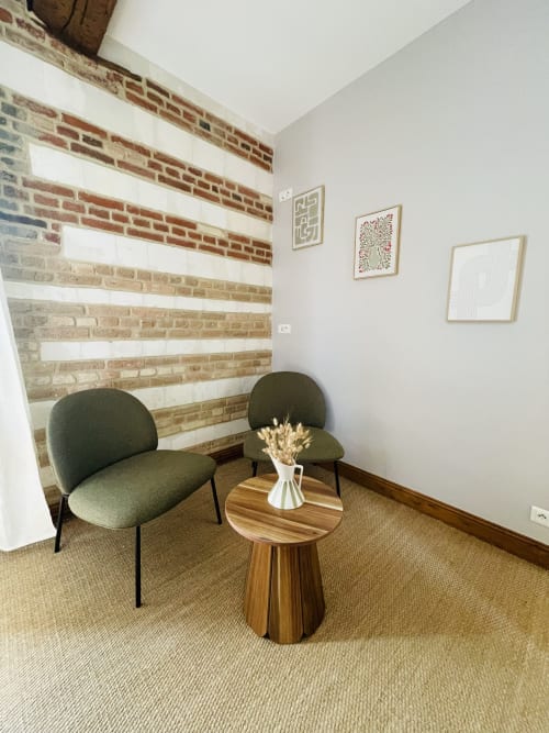 Espace lounge contemporain de la suite Maison Nolette avec fauteuils verts, table en bois et mur de briques à motifs rayés