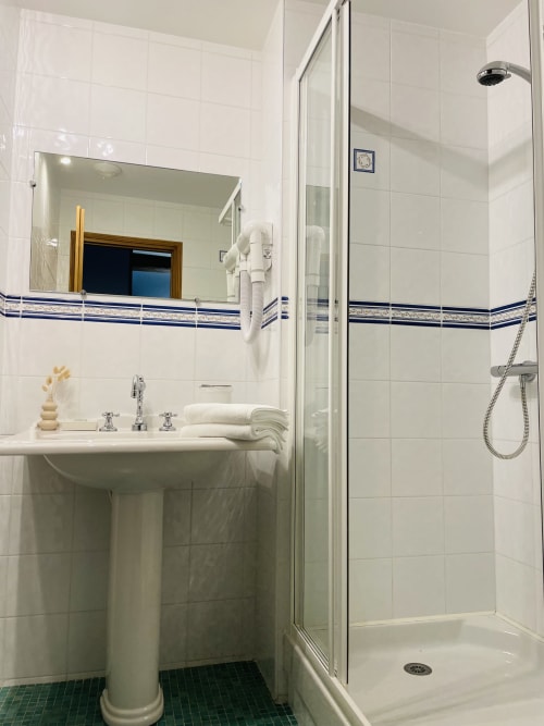Salle de bains moderne et épurée à la Maison Nolette avec lavabo sur colonne, douche à l'italienne et accents de carrelage bleu