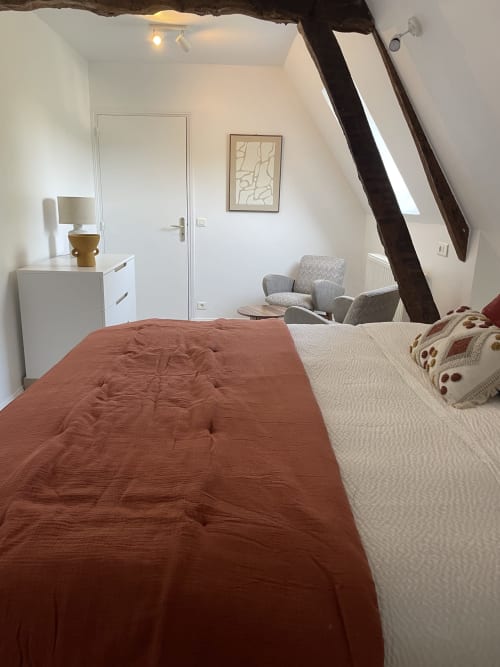Chambre lumineuse sous les combles de la Maison Nolette avec literie terre cuite, poutres apparentes, coin détente et mobilier blanc