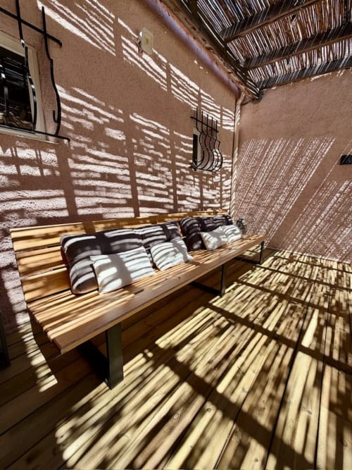Terrasse ensoleillée de la villa Casa A Stonda à Porto-Vecchio avec banc en bois, coussins rayés et ombrage aux motifs de feuilles de palmier