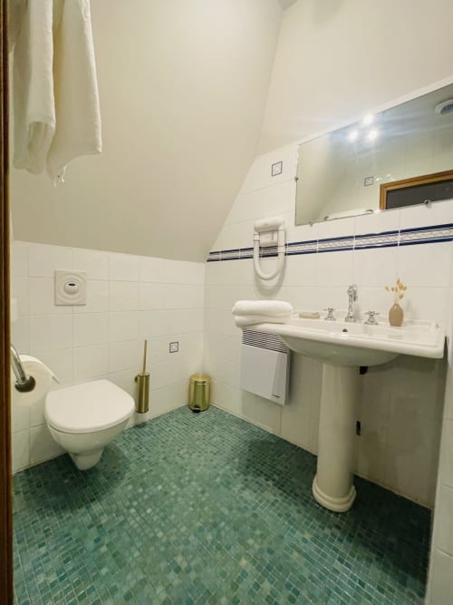 Salle de bain de la Maison Nolette avec lavabo sur piédestal, toilettes murales, carrelage vert et serviettes blanches au gîte Noyelles sur Mer