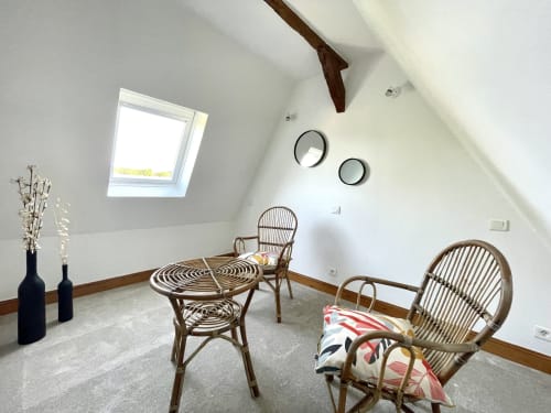 Chambre mansardée lumineuse à la Maison Nolette avec fauteuils en rotin, table ronde, puits de lumière et vue sur le jardin