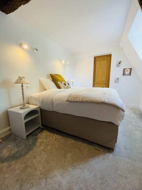 Chambre lumineuse de la Maison Nolette B&B avec lit, table de nuit blanche, lampe et porte en bois à Noyelles sur Mer