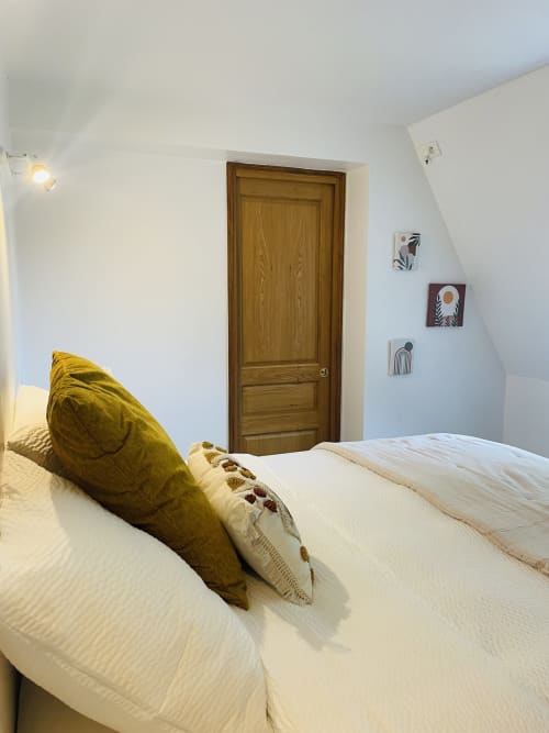 Chambre accueillante à la Maison Nolette B&B à Noyelles sur Mer avec literie blanche, coussin moutarde, porte en bois et décoration murale