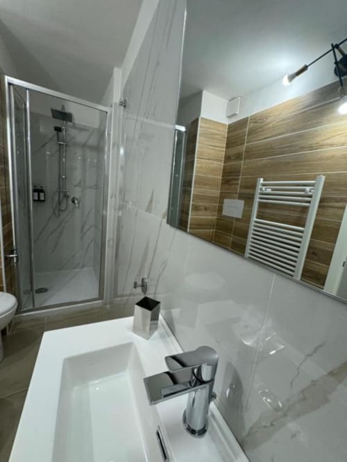 Bagno moderno in appartamento a Reggio Calabria con lavabo bianco, rubinetto cromato, doccia in vetro, parete con piastrelle in legno e