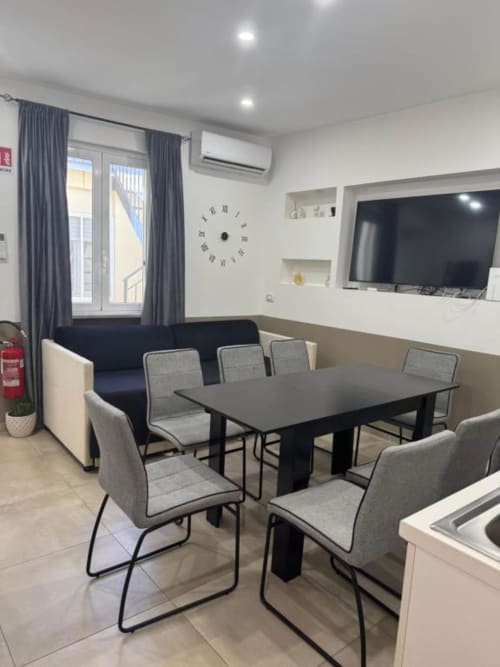 Zona living moderna con tavolo da pranzo, sedie grigie, divano, TV a schermo piatto e accesso al balcone a Maison ì Room in