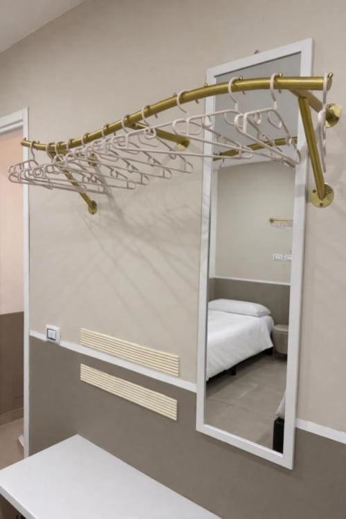Appendiabiti in ottone con grucce bianche in camera da letto di moderno appartamento a Reggio di Calabria, specchio con cornice bianca e porta