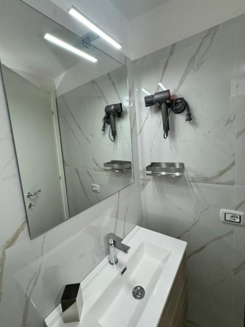 Moderno bagno della Maison ì Room a Reggio di Calabria con pareti in marmo, lavabo bianco, specchio e asciugacapelli a muro