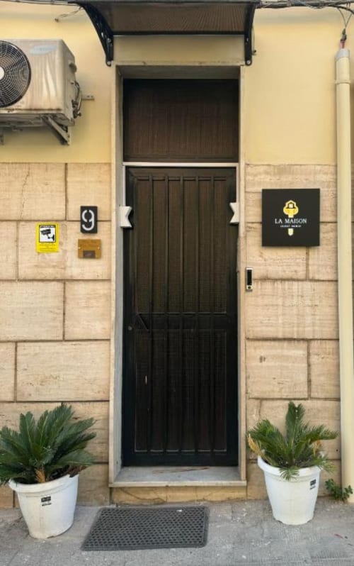 Ingresso con porta in legno nero a La Maison room, suite & apartment a Reggio di Calabria, decorato con piante in vaso e arredi color crema