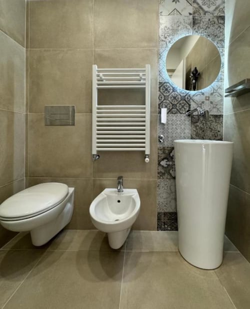 Bagno moderno in appartamento a Reggio di Calabria con wc, bidet, lavabo su piedistallo, scaldasalviette e specchio rotondo