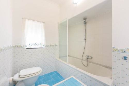 Bagno luminoso dell'appartamento Il Poeta a Procida con pareti bianche, accenti in piastrelle blu, toilette e doccia con box in vetro
