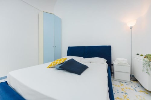 Camera da letto moderna con letto blu navy, biancheria bianca e cuscino giallo presso IL POETA, Procida